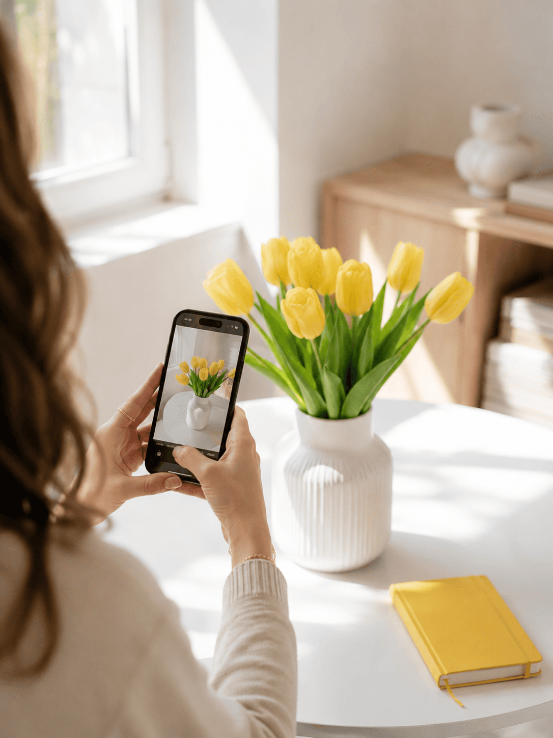 Hände fotografieren mit dem Smartphone gelbe Tulpen in weißer Vase auf hellem Tisch, Content-Erstellung mit dem Handy
